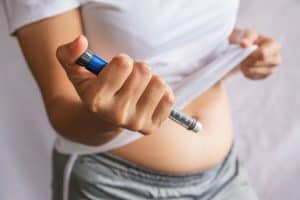 a person prepares to inject themselves in the abdomen. Ozempic is a glp-1 drug that is typically injected into subcutaneous fat.